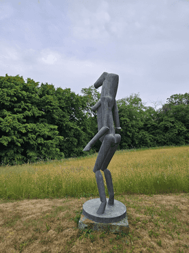 Das Kunstwerk aus Bronze steht auf einer Grünfläche bei dem Hof von Fritz Koenig 